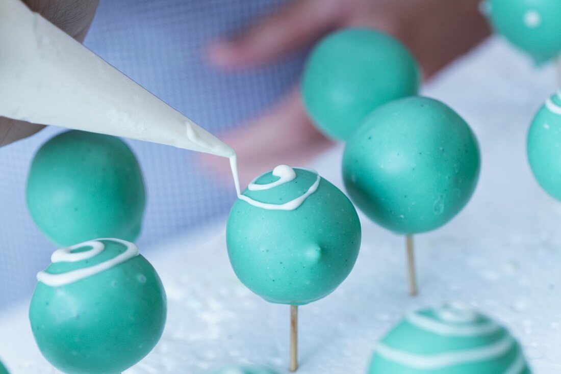Turquoise coloured cake pops being decorated with white icing