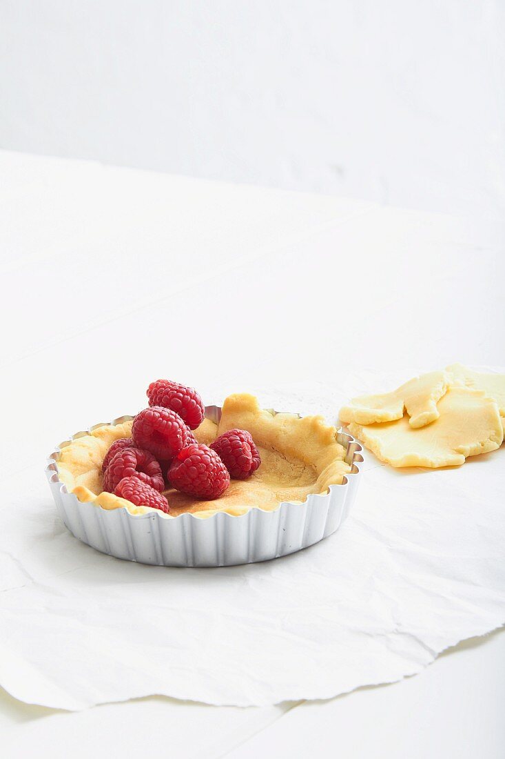 Unbaked shortcrust pastry in a tartlet dish with fresh raspberries