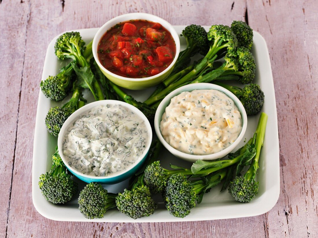 Various dips (salsa, raita, and a cheese and chive dip) with broccoli