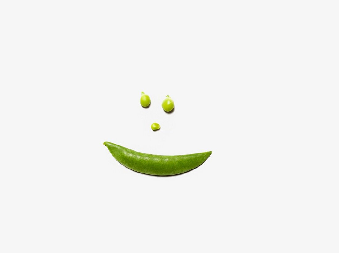 A smiley face made from a pea pod and peas