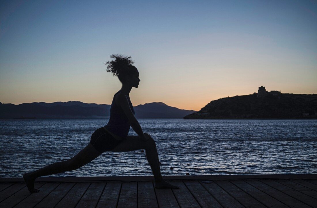 Junge Frau beim Yoga im Abendlicht am Meer