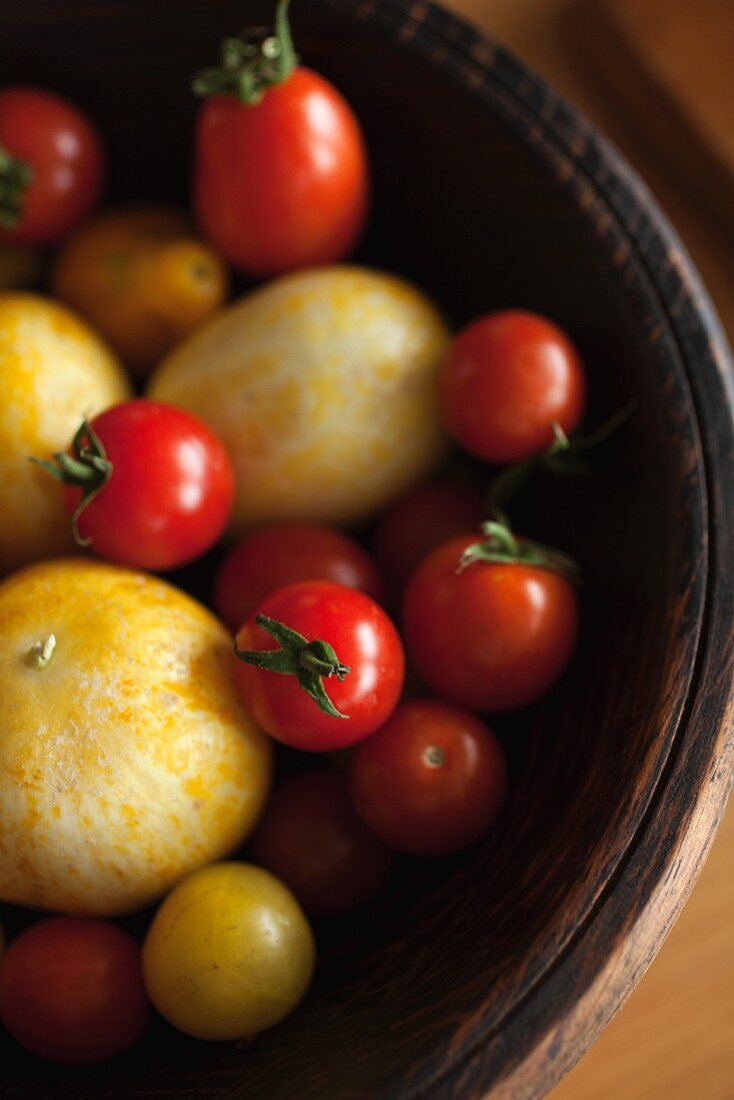 Red and yellow tomatoes with lemon cucumbers in a wooden bowl