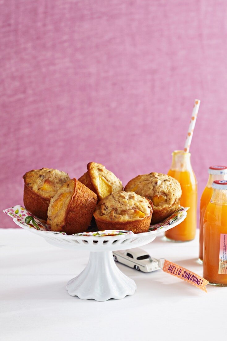 Peach muffins on a cake stand next to bottles of peach juice