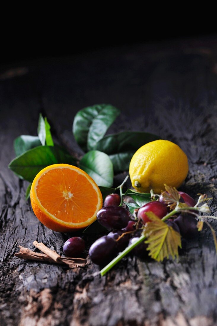 Stillleben mit halber Orange, Zitrone, roten Trauben und Zimtstangen auf Baumrinde