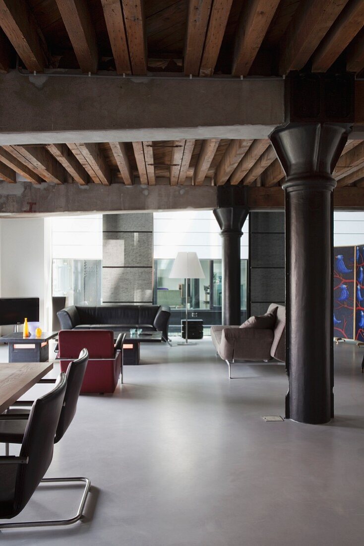 Loft apartment with black metal pillar under girder structure, dining area to one side and lounge area with retro armchairs and sofa