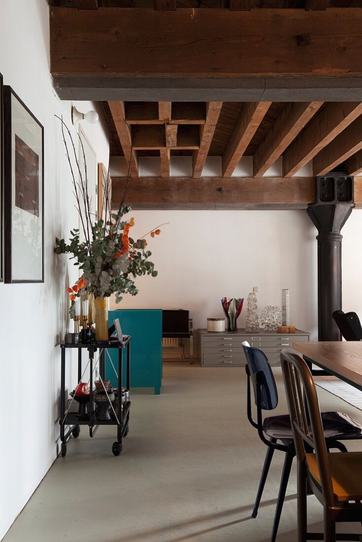 Retro chairs in loft-style interior with rustic wood-beamed ceiling and black metal column in background