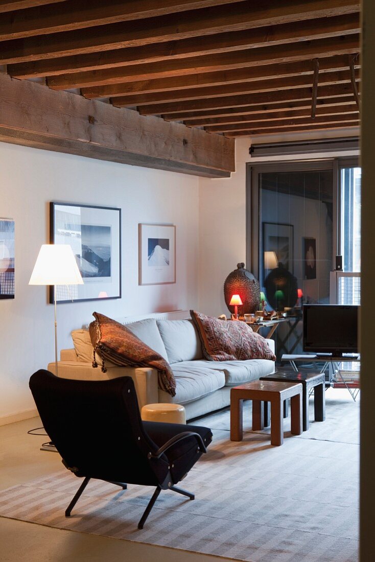 Schwarzer Retro Sessel und Sofa um rustikale Couchtische in loftartiger Wohnung mit Holzbalkendecke