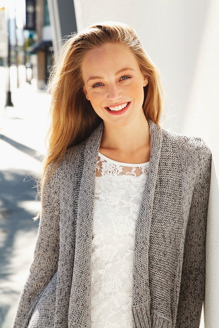 A young blonde woman wearing a white lace blouse and a grey cardigan