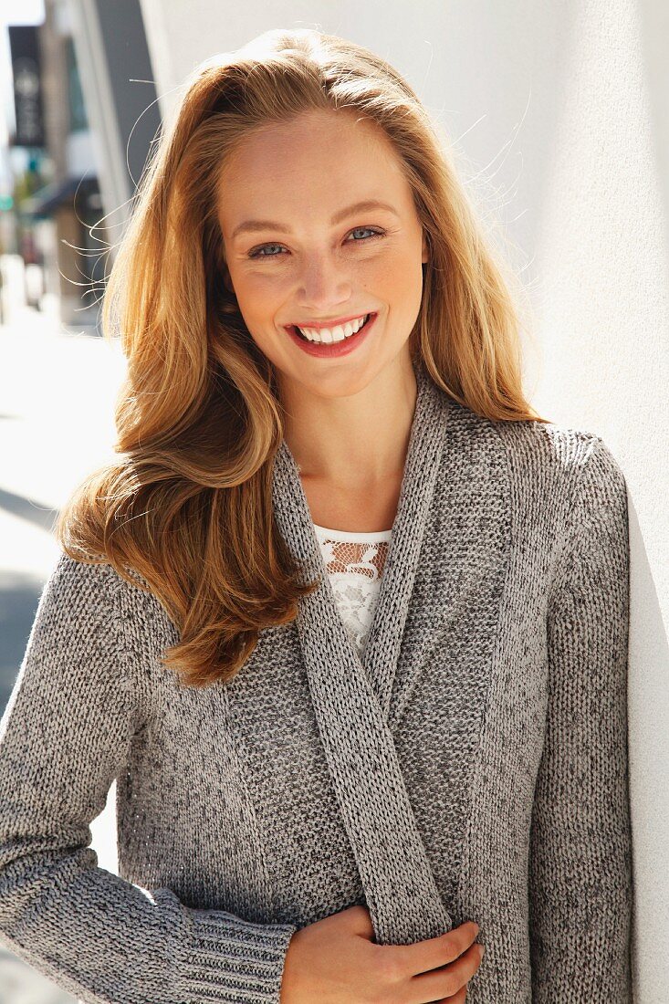 A young blonde woman wearing a white lace blouse and a grey cardigan