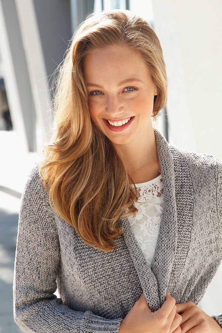 A young blonde woman wearing a white lace blouse and a grey cardigan