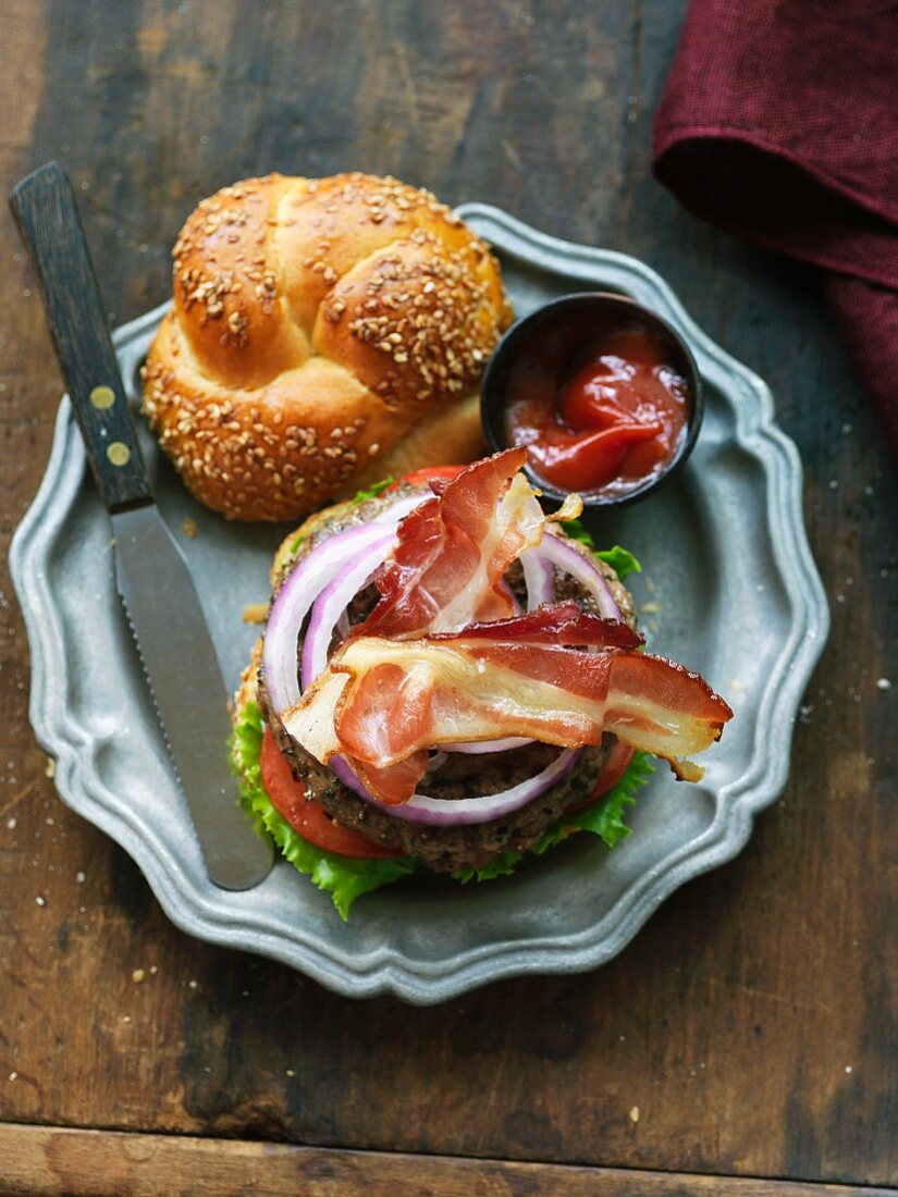 A hamburger with bacon, lettuce, tomatoes on a pewter plate (seen from above)