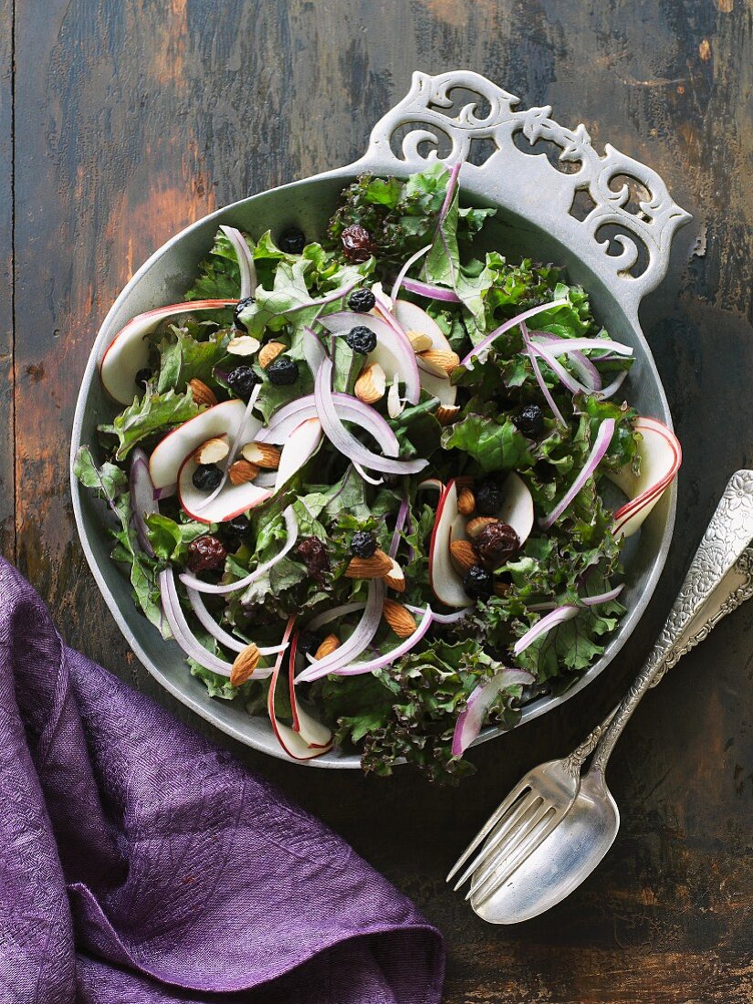 Kale salad with dried berries and almonds in a pewter bowl