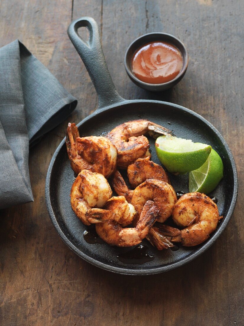 Blackened shrimps in a pan with lime wedges