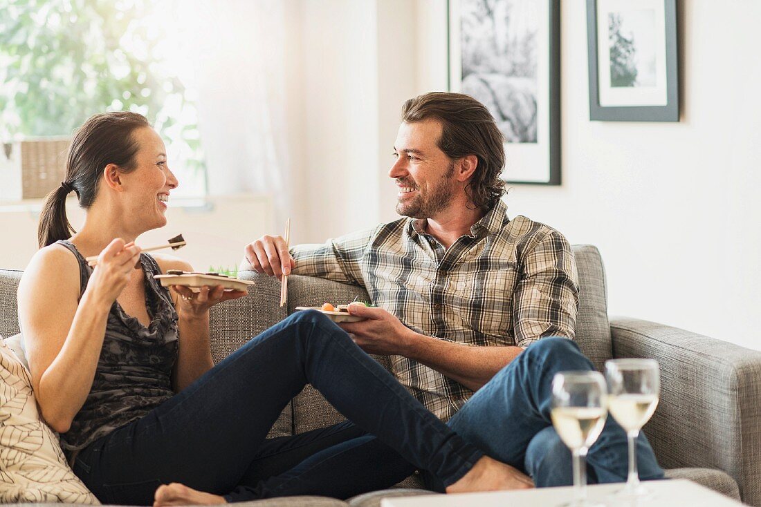 A couple eating, sitting comfortably on a sofa