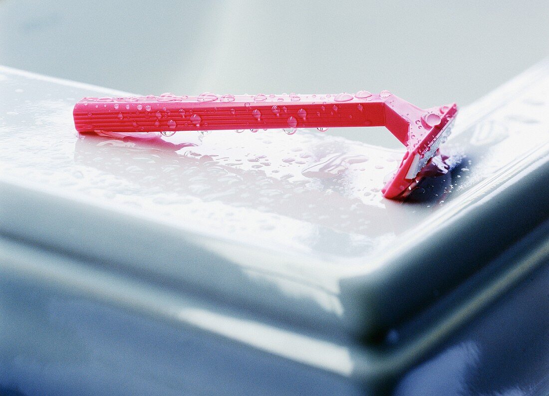 A red disposable razor on the edge of a bathtub