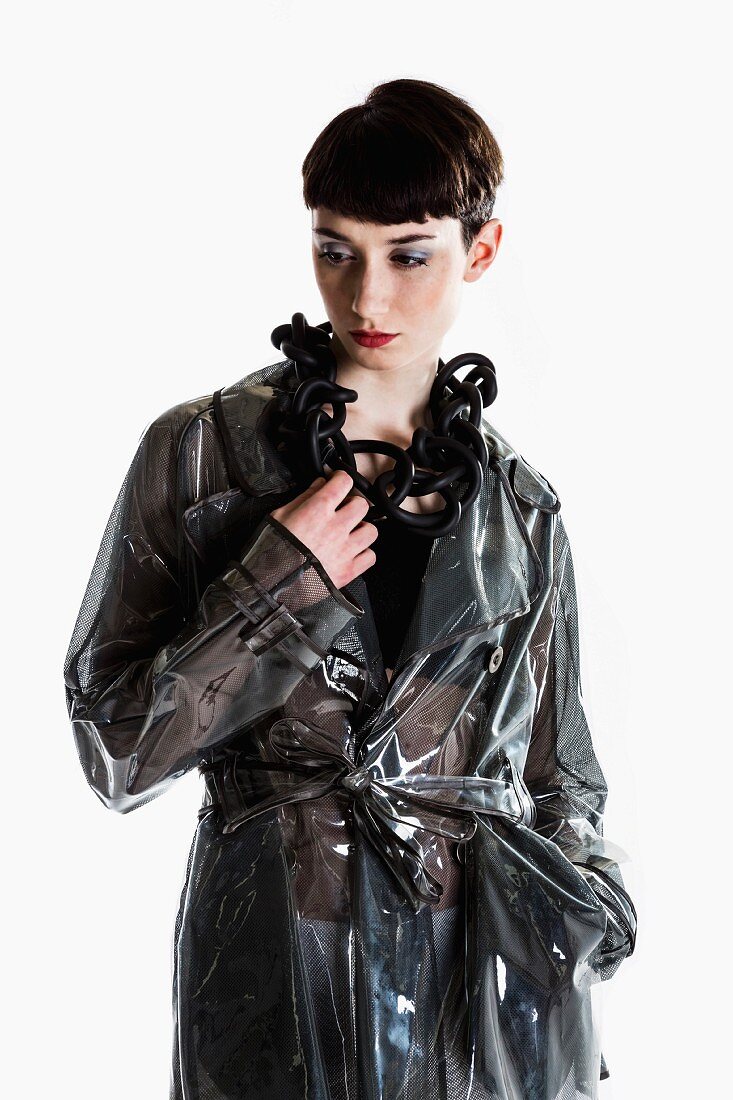 A young woman with a garcon haircut wearing a black, transparent rain coat and jewellery