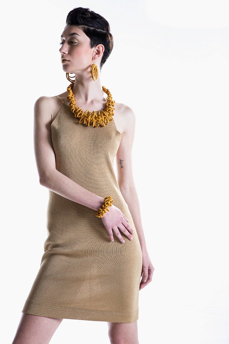 A young woman wearing a gold coloured Lurex knitted dress with yellow jewellery
