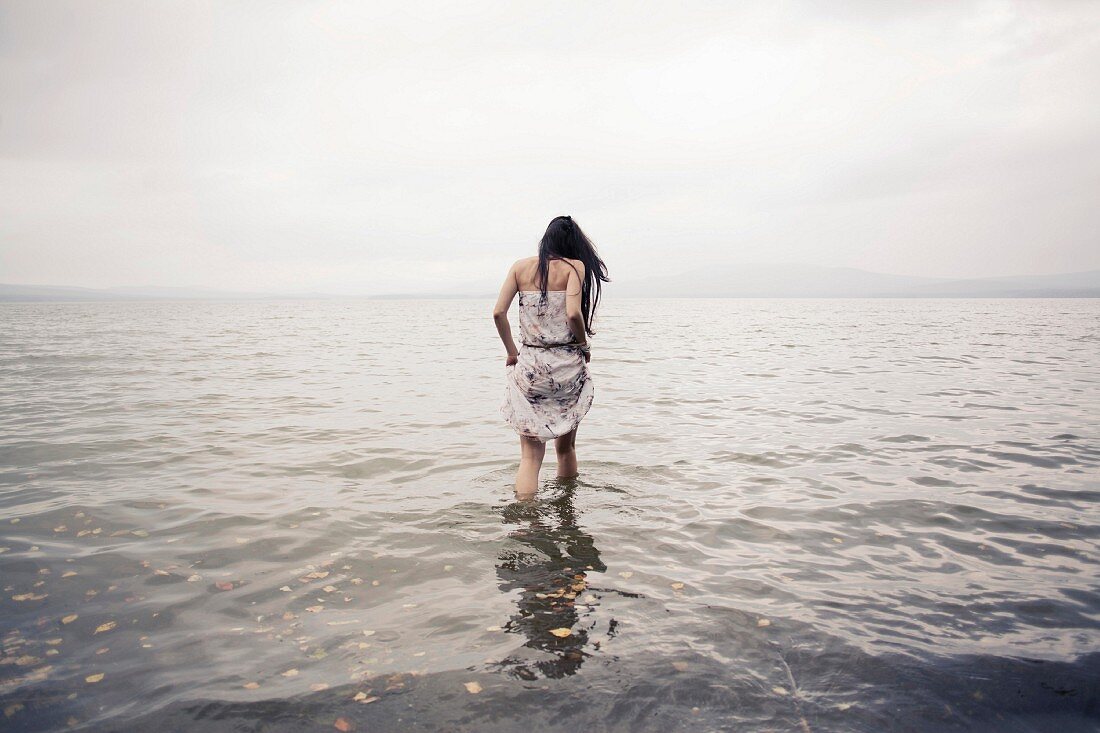 Frau im Sommerkleid läuft am Strand durchs Wasser