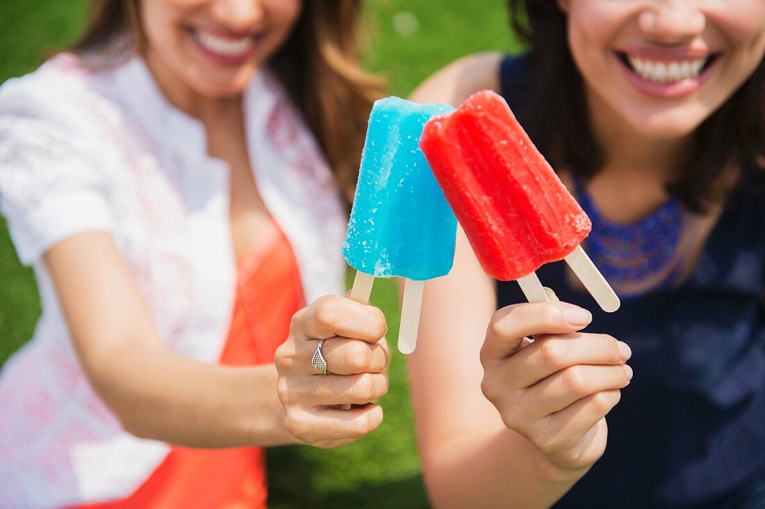 Zwei junge Frauen halten buntes Eis am Stiel in der Hand