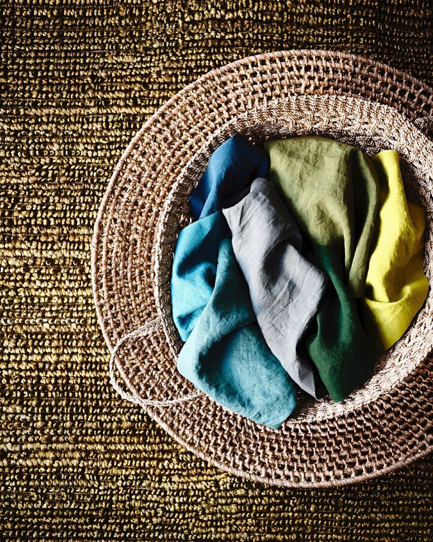 Colourful fabrics in seagrass basket on woven mat and silvery-green structured carpet