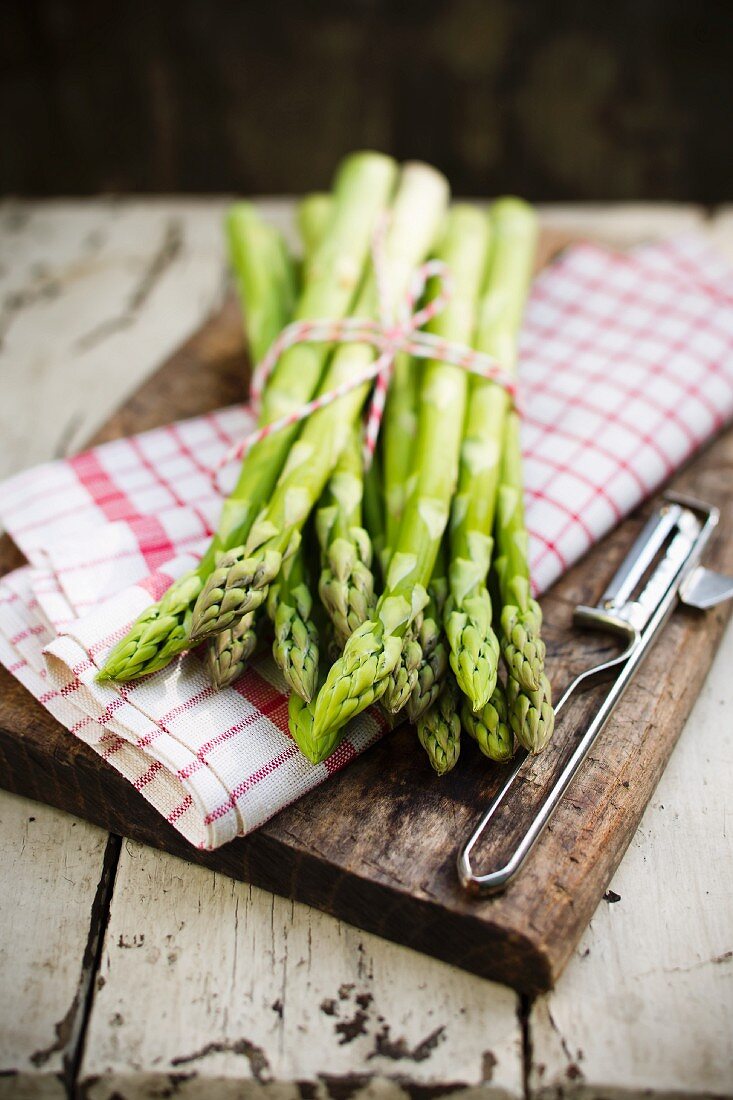A bundle of green asparagus with a tea towel on a chopping board