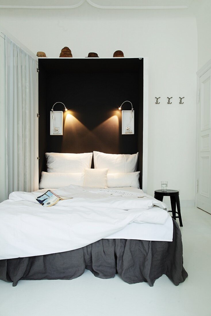 Foldaway bed with dark grey valance and white bed linen against black wall with reading lamps