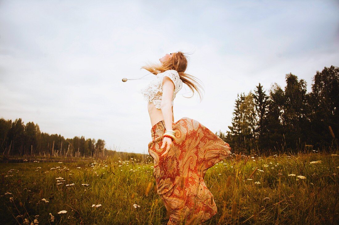 A young blonde woman wearing hippie-style clothing dancing over a meadow