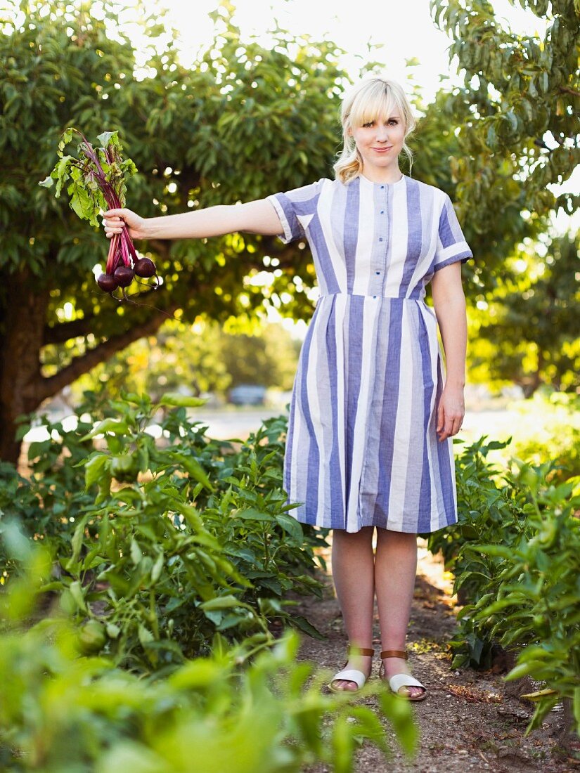 Blonde woman wearing striped dress holding freshly harvested beetroots
