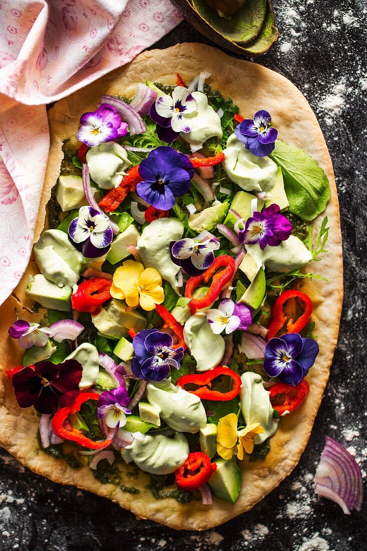 Avocado salad with edible flowers, peppers, red onions and lettuce on a blind-baked pizza base