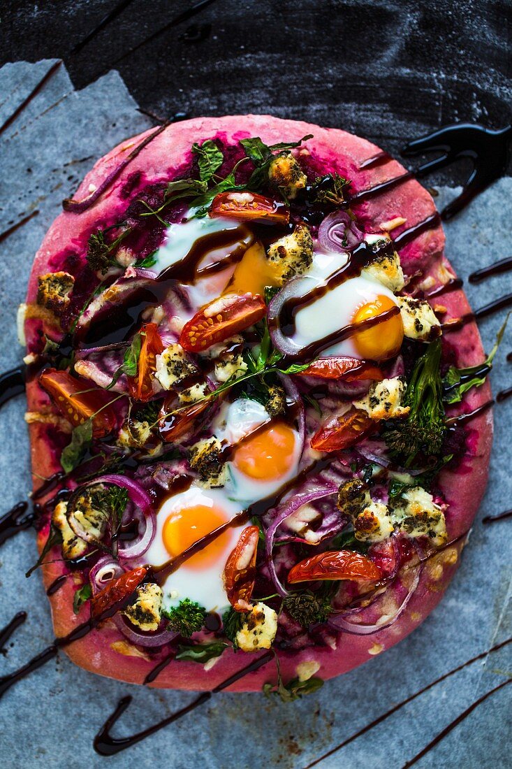 Beetroot pizza dough with broccolini, red onions, tomatoes, goat's cheese, rocket, cheese, fired eggs and balsamic cream