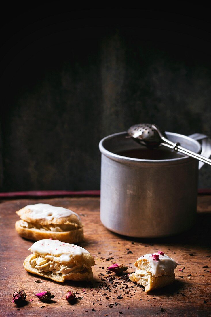 Mini eclairs, whole and half-eaten, next to a cup of tea on a wooden table