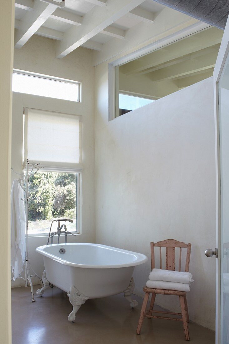 Free-standing, vintage bathtub next to window and below transom window in interior wall
