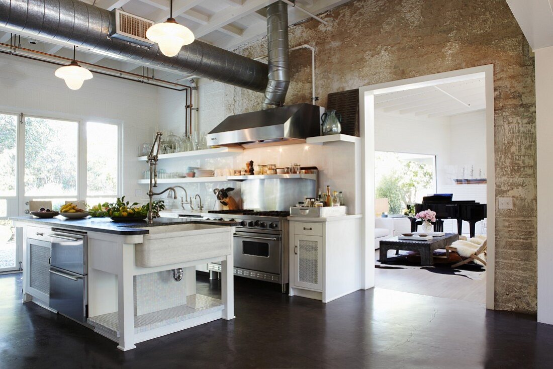 Free-standing counter in open-plan kitchen below ventilation ducts; wide, open doorway with view into living room