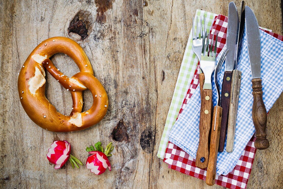 A pretzel, radishes and rustic cutlery (seen from above)