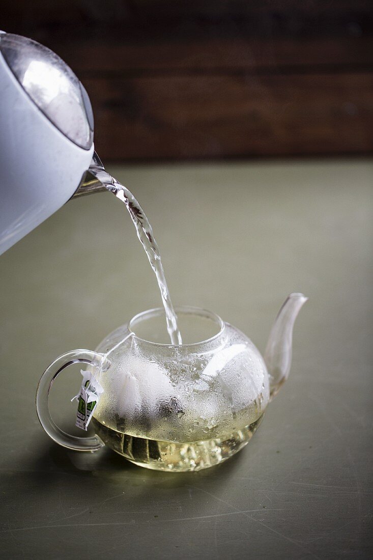 Hot water being poured into a teapot with tea bags