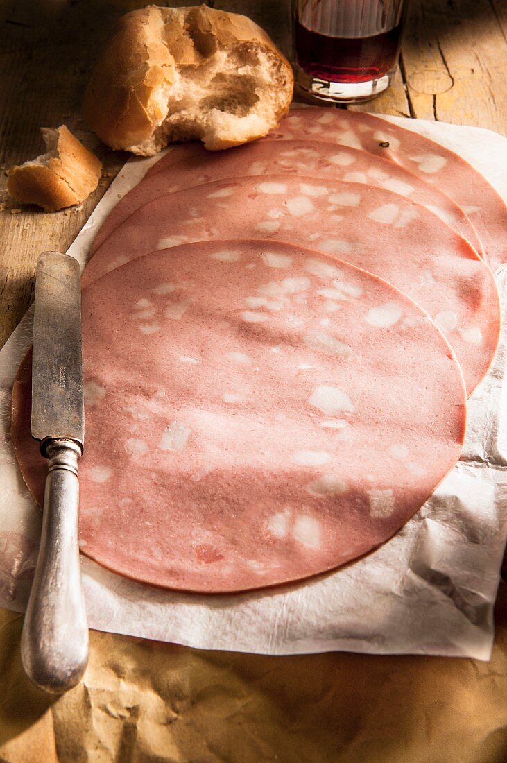 Slices of mortadella on a piece of papers with bread and red wine