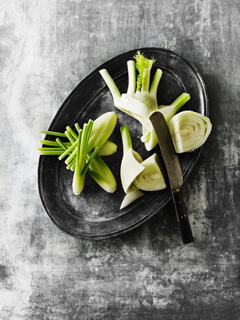 Sliced fennel bulbs with a knife on a grey platter