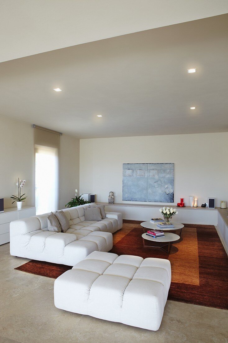 Interior with white sofa combination, rug in shades of brown and ornaments on masonry shelf running around two walls