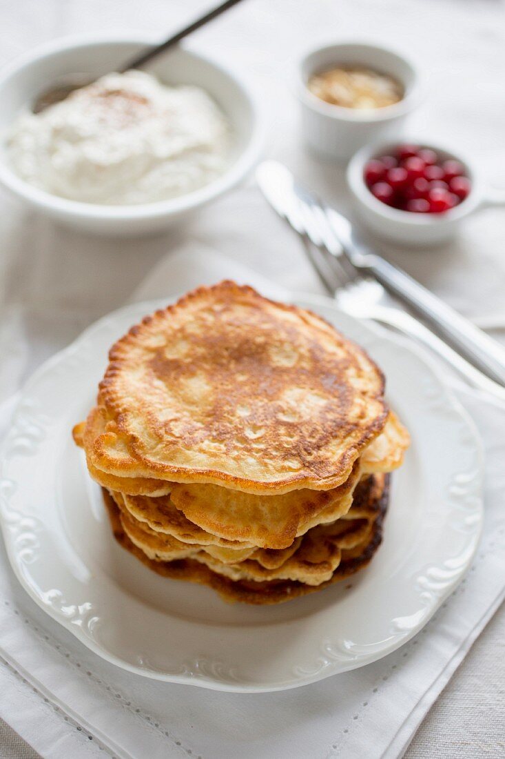 Gestapelte Pancakes vor Kokos-Zimt-Quark, roten Johannisbeeren und Mandelblättchen