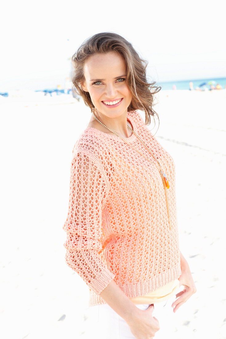 Junge Frau in apricotfarbenem Sommerpulli am Strand