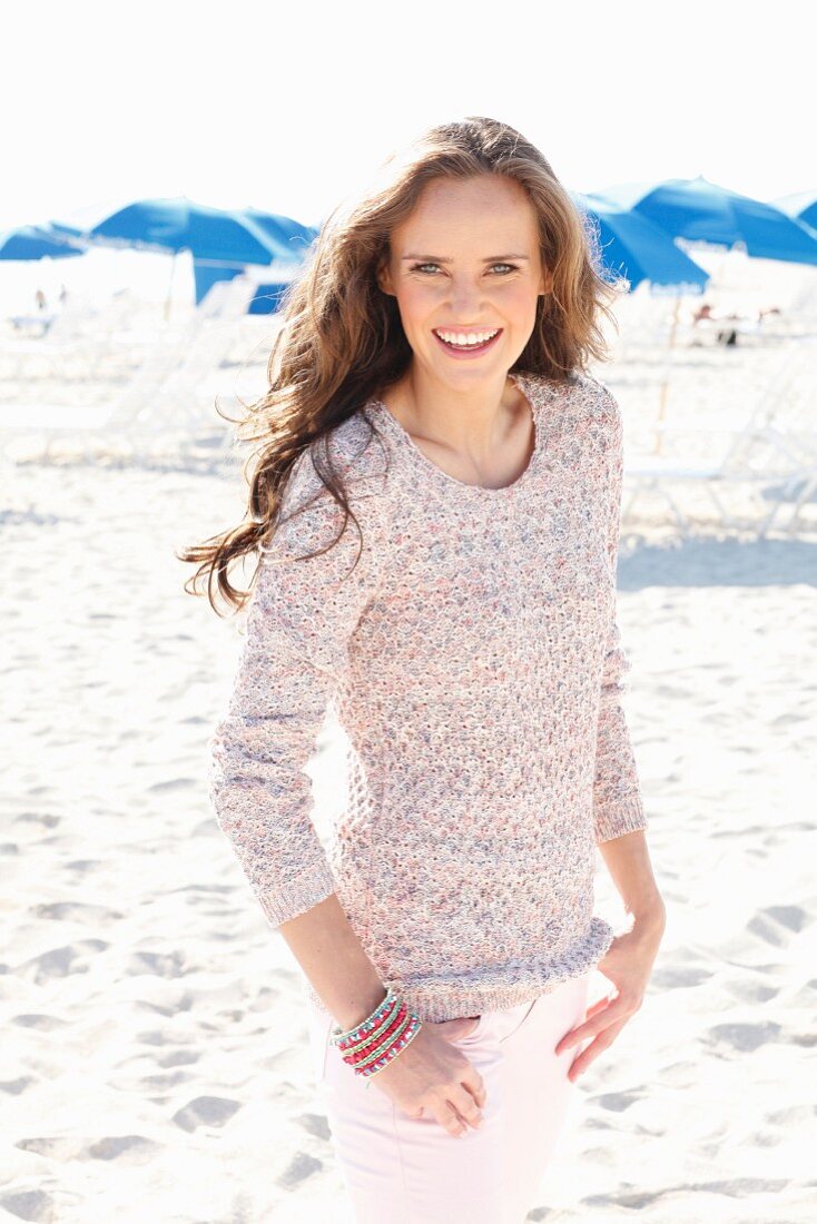 Junge Frau mit langen Haaren in gestricktem Pulli am Strand