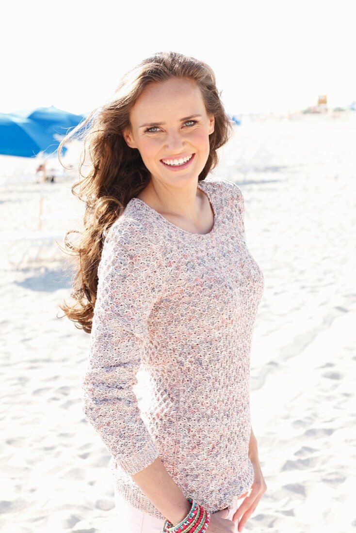 A young, long-haired woman on a beach wearing a knitted jumper