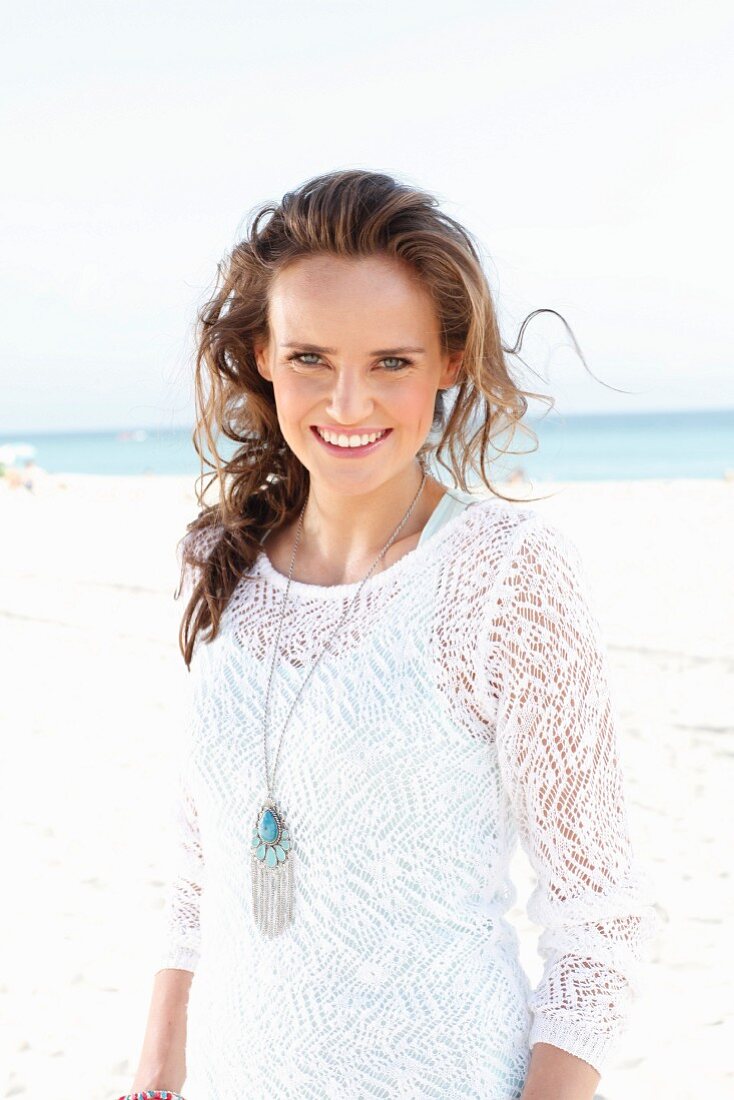 A young, long-haired woman on a beach wearing a white lace dress