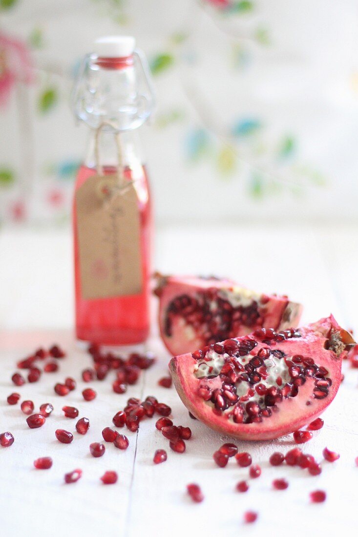 A bottle of pomegranate juice, sliced pomegranate and pomegranate seeds