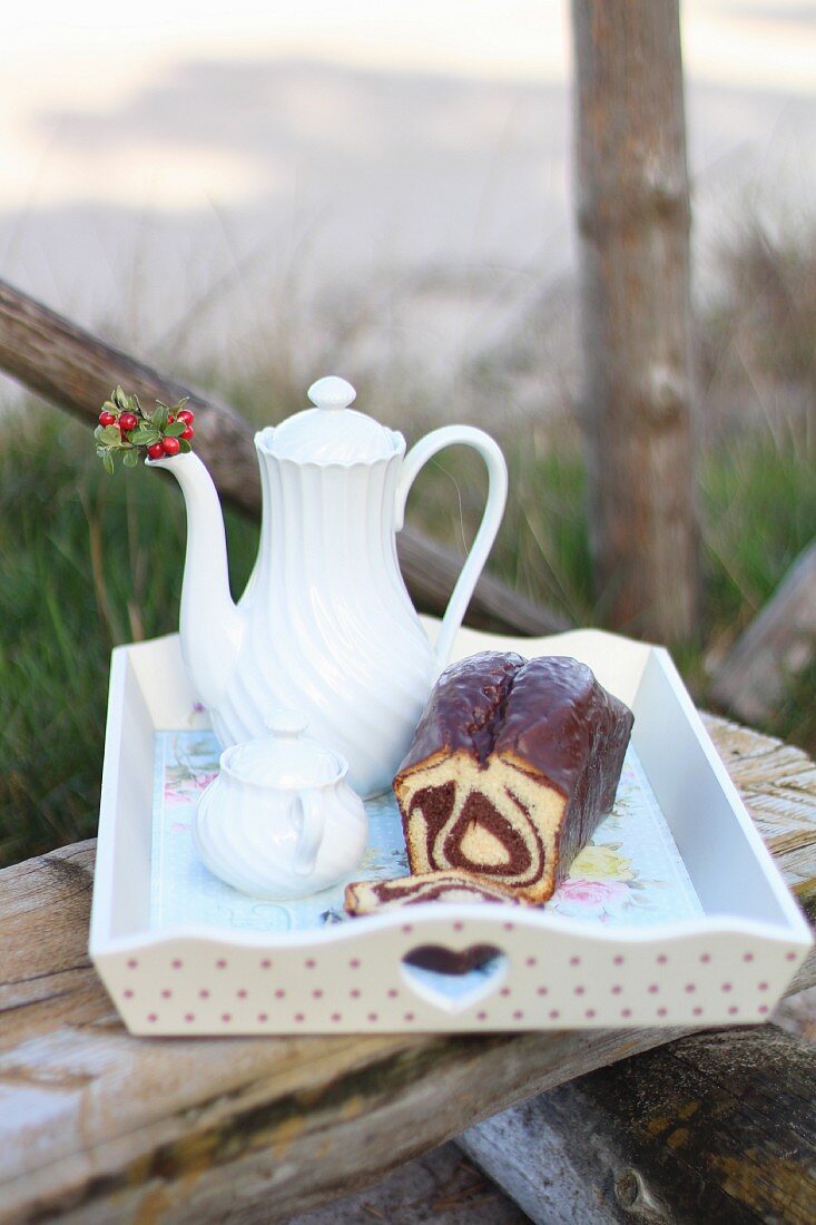 Tablett mit Marmorkuchen und Kaffee auf Holzbank im Garten