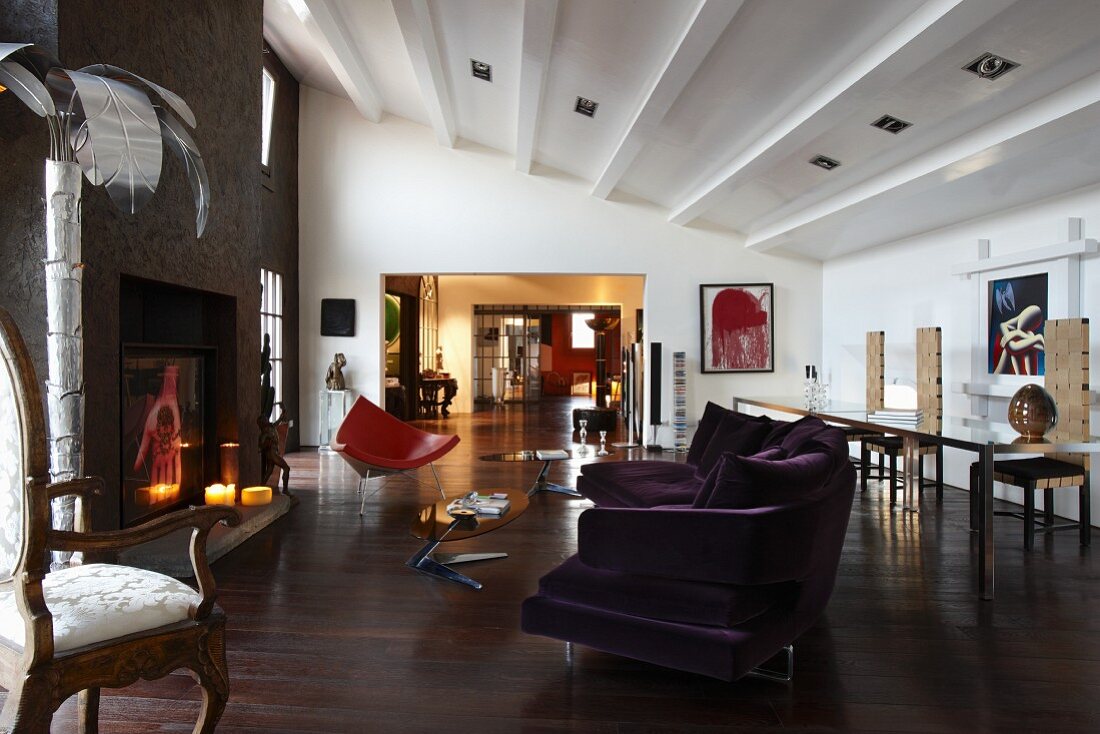 Open-plan, eclectic interior of loft apartment with modern sofa, Rococo armchair and open fireplace
