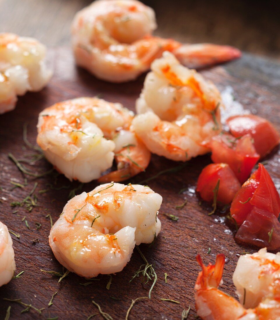 Fried shrimps, tomatoes and herbs on a wooden surface