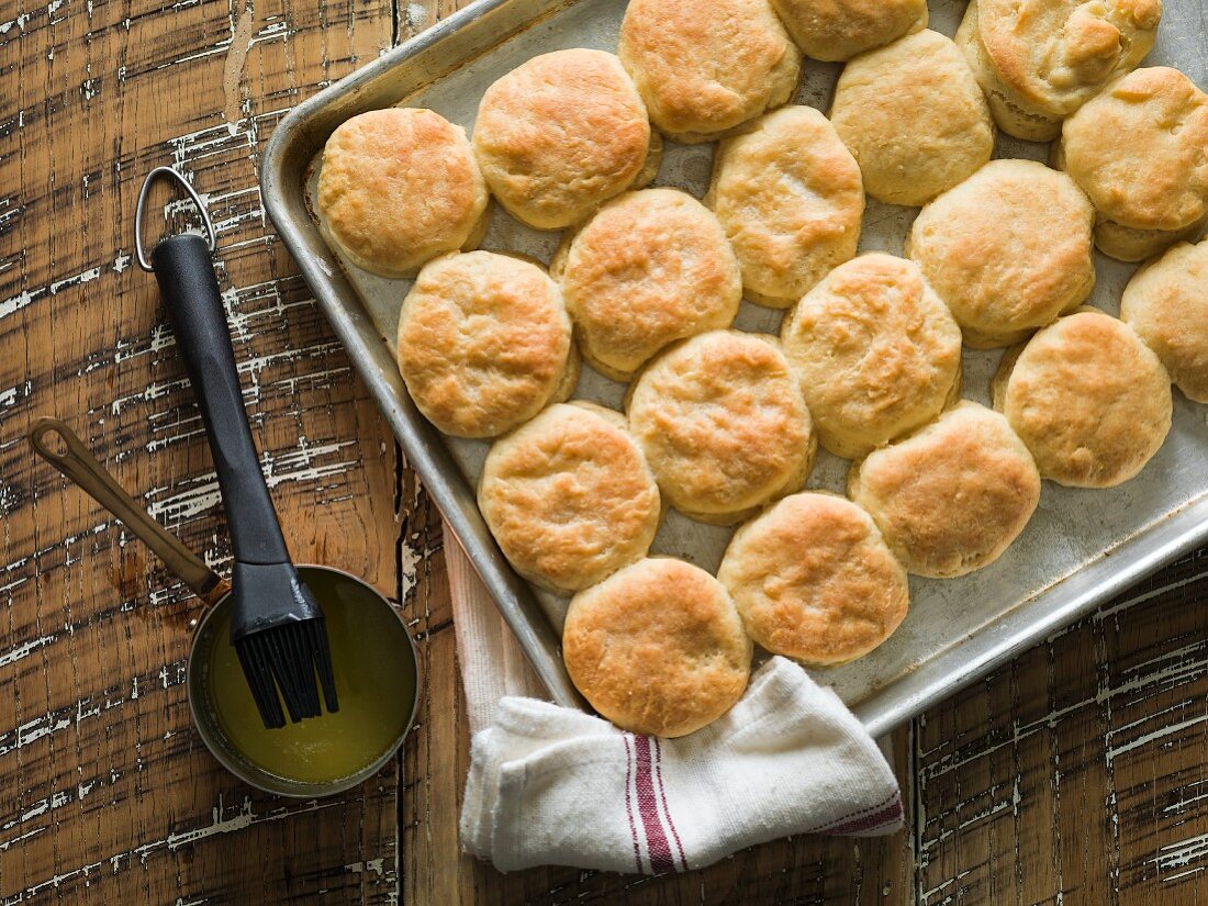 Buttermilch-Biscuits auf Backblech, daneben zerlassene Butter und ein Backpinsel
