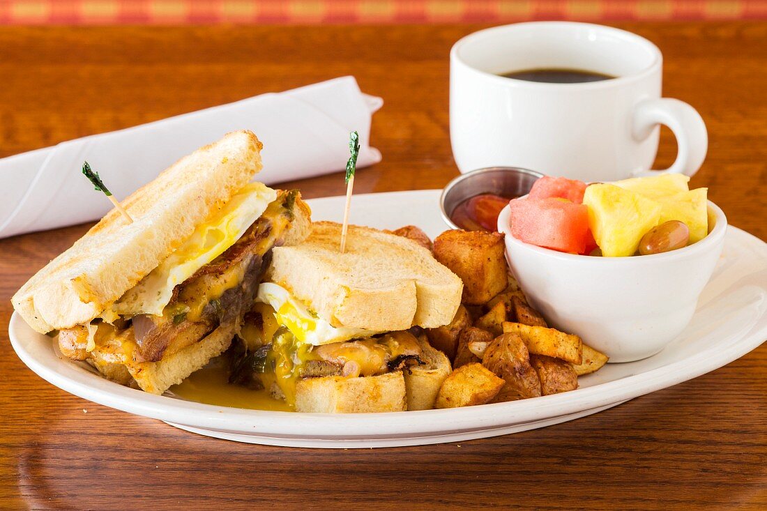 A breakfast sandwich with fried potatoes, fruit salad and coffee