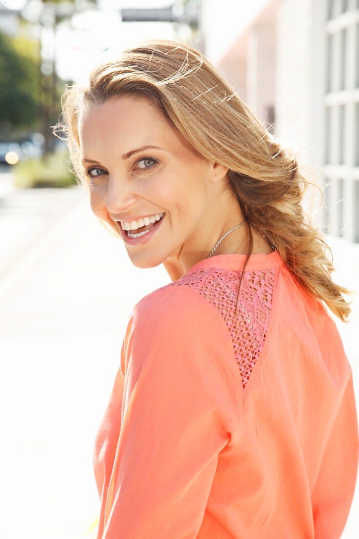 A young blonde woman wearing a salmon pink blouse